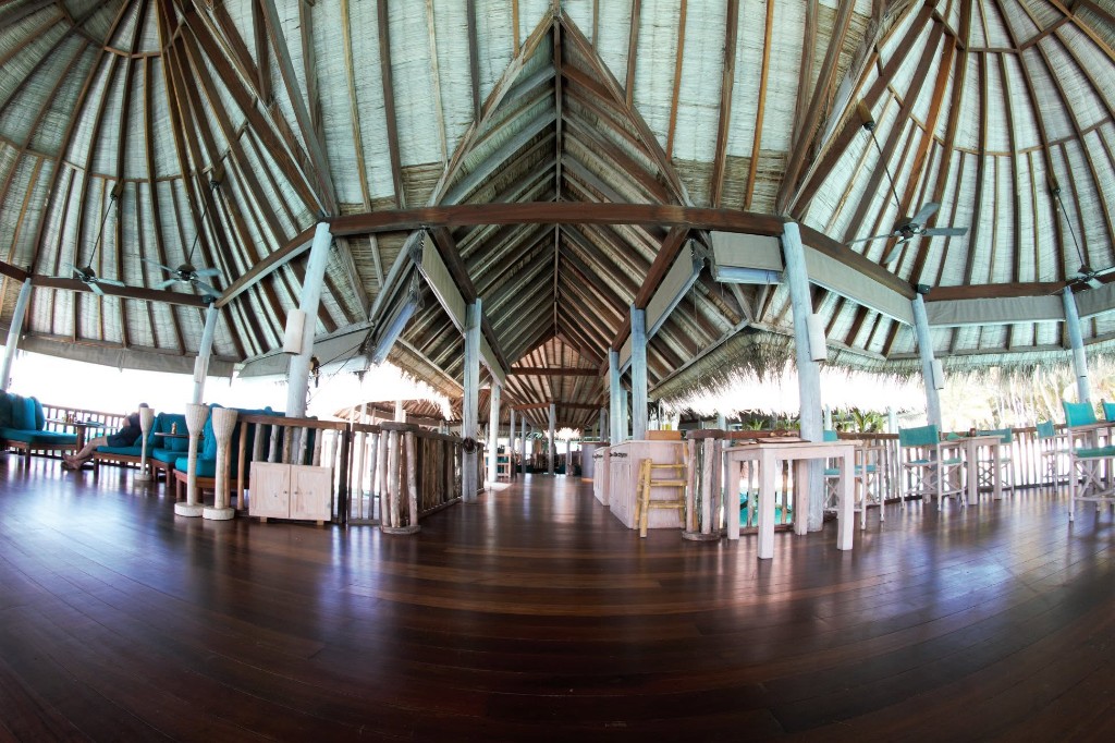Open-air resort lobby with thatched roof and teal lounge seating